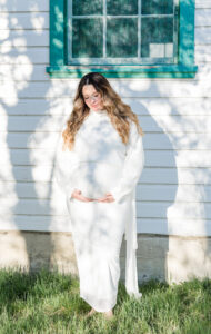 A mom holding her pregnant belly with a green window in the background 