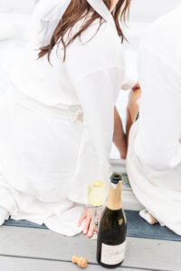 A bride and groom holding hands with champagne, a glass, and a cork on the ground 
